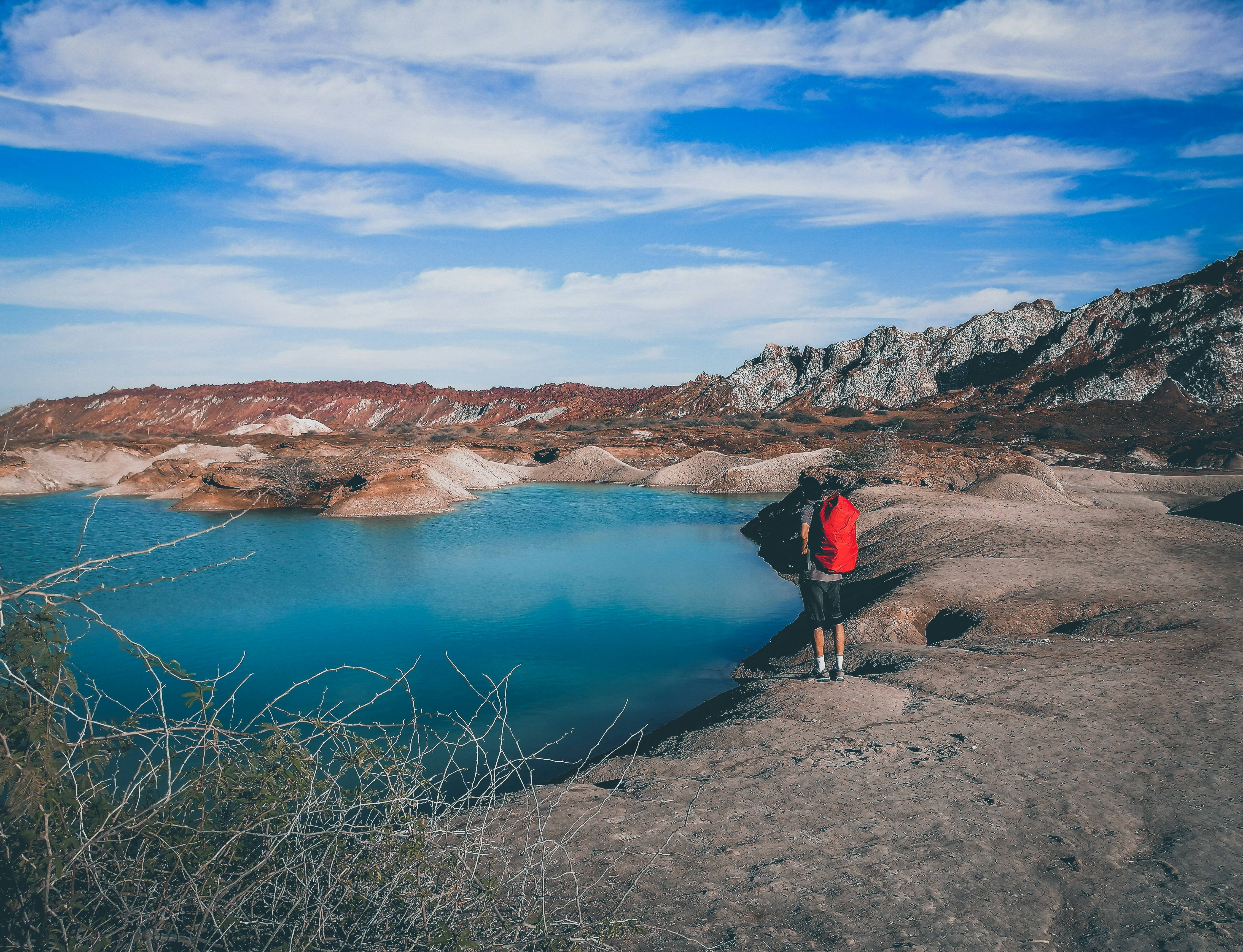 man in black jacket standing on brown rock near lake during daytime